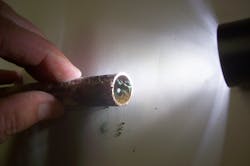 Figure (1): A view of a pinhole in copper domestic water piping. Pinhole leaks occur at a sacrificial anode, in particular when the protected cathode area is large compared to the sacrificial anode area. This piping was part of a jail domestic water system. Figure (1): A view of a pinhole in copper domestic water piping. Pinhole leaks occur at a sacrificial anode, in particular when the protected cathode area is large compared to the sacrificial anode area. This piping was part of a jail domestic water system.